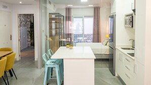 A modern kitchen with a central island, a dining area with yellow chairs, and a view of a balcony with a table and chairs.