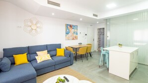 A modern living room with a blue sofa, yellow cushions, a round coffee table with plants, and a dining area with yellow chairs.