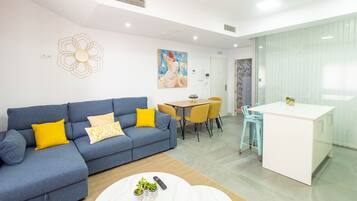 Een moderne woonkamer met een blauwe bank, gele kussens, een ronde salontafel met planten, en een eethoek met gele stoelen.