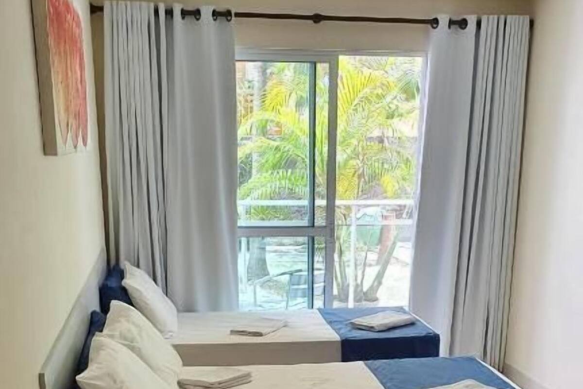 A hotel room with two beds, a small table, and a window with curtains.