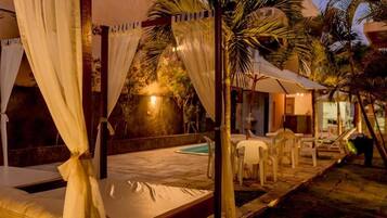 Uma cama com cortinas brancas, piscina e área de estar externa.