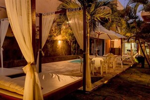 Un letto con tende bianche, una piscina e un'area relax all'aperto.