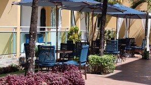 A poolside area with blue chairs and umbrellas, surrounded by plants and a pool. - Pousada Agua Viva (Ipojuca)
