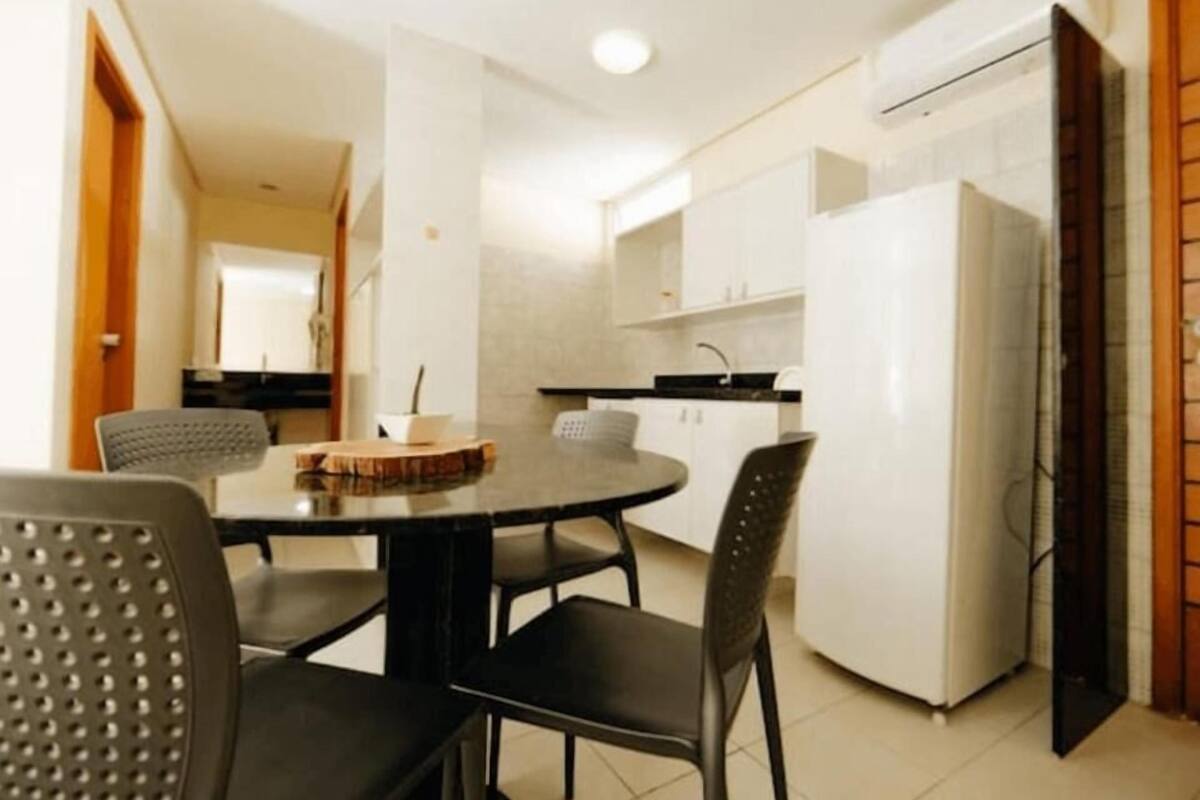 A compact kitchen with white cabinets, a black countertop, and a refrigerator. There is a dining table with four chairs.