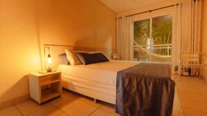 A hotel room with a bed, nightstand, and a view of the outdoors through a large window. - Pousada Agua Viva (Ipojuca)