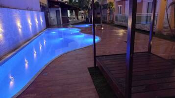 Una piscina con iluminación azul, rodeada por una terraza de madera y palmeras.