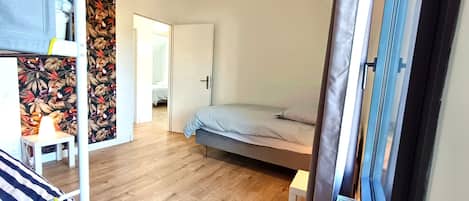 Een slaapkamer met een bed, een klein tafeltje en een kledingkast. Er is een deur die naar een andere kamer leidt.