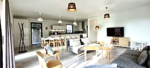 A modern living room with a sofa, chairs, a dining area, and a kitchen in the background.