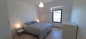 Une chambre à coucher comprenant un lit, des tables de chevet, un luminaire suspendu, une fenêtre et un radiateur.