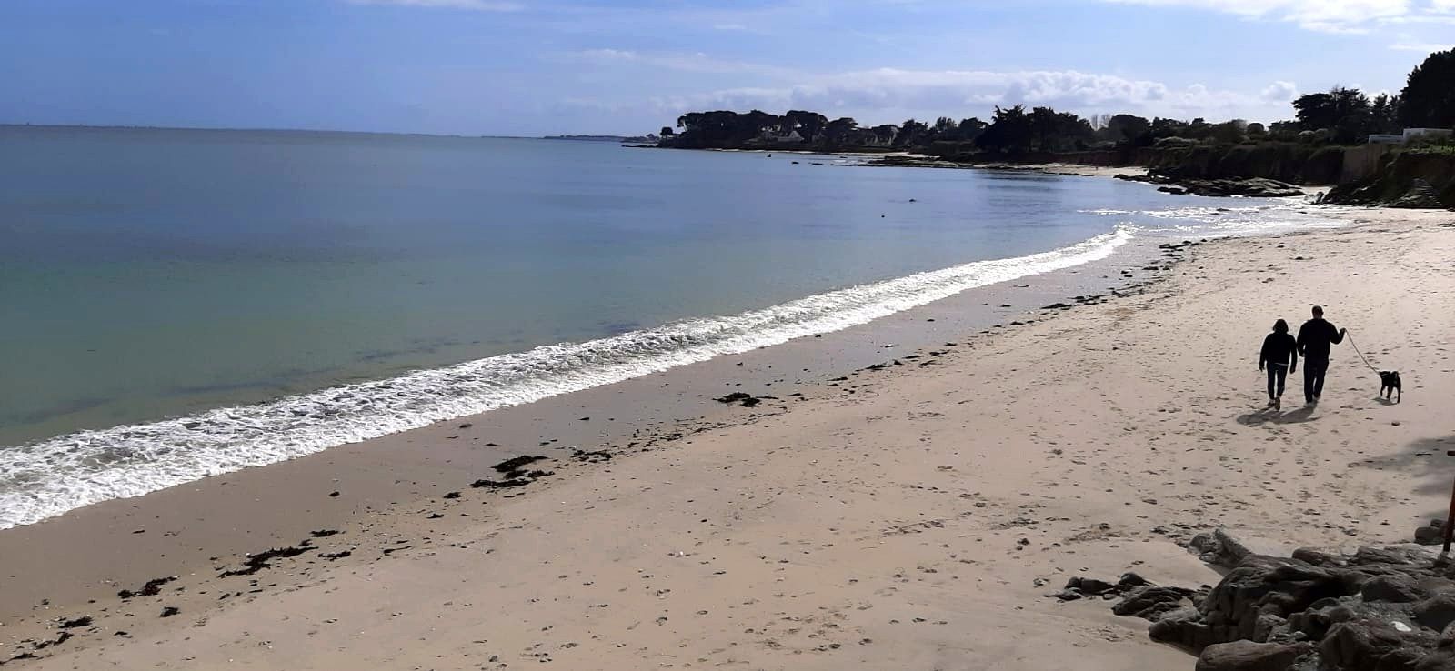 A beach with a clear sky, calm sea, and rocky outcrops.