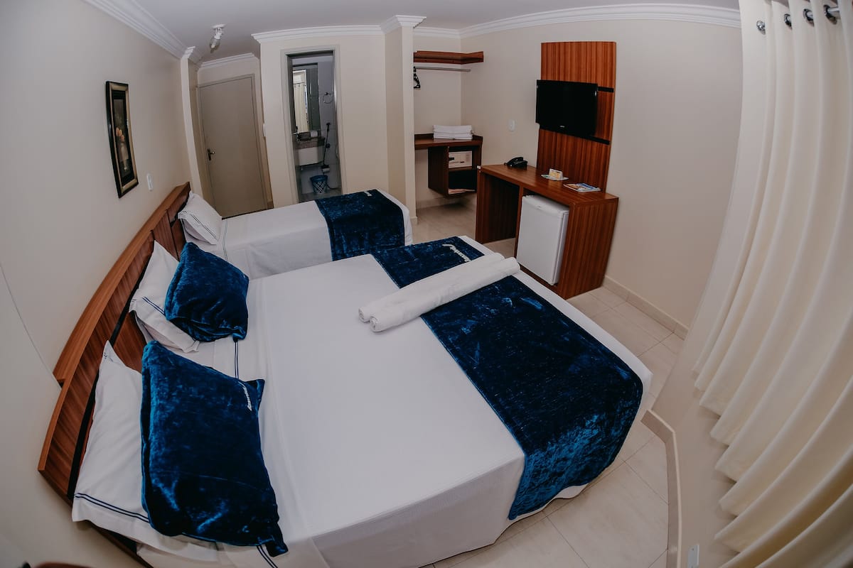 A hotel room with two beds, a desk, a TV, and a bathroom visible through an open door.