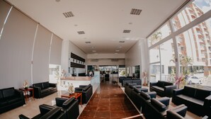 A spacious lobby with black leather sofas, a reception desk, and large windows offering a view of the city. - Imperio Romano Thermas Hotel -BVTUR (Caldas Novas)