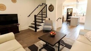 A living room with a sofa, a coffee table, a TV, and a staircase. - Comfy Cherry Blossom Townhouse / Easy DC Access (Washington)