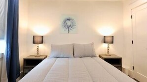 A bedroom with a large bed, two bedside tables, a wall-mounted lamp, and a window with curtains. - Comfy Cherry Blossom Townhouse / Easy DC Access (Washington)