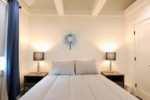 Camera da letto con un letto grande, due comodini, una lampada a parete e una finestra con tende.