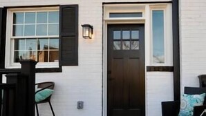 A white building with a dark front door, a window with shutters, and a porch with a chair. - Comfy Cherry Blossom Townhouse / Easy DC Access (Washington)