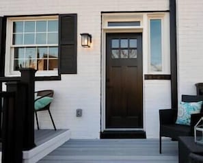 Un edificio bianco con una porta d'ingresso scura, una finestra con persiane e un portico con una sedia.