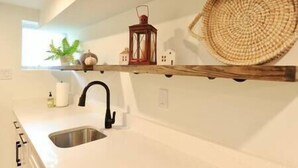 A kitchen with a white countertop, a stainless steel sink, a black faucet, a woven basket, a lantern, and a small house decoration. - Comfy Cherry Blossom Townhouse / Easy DC Access (Washington)