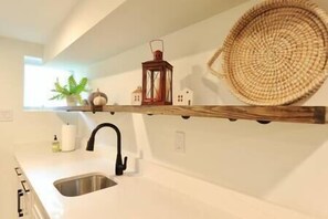 Una cucina con un piano di lavoro bianco, un lavello in acciaio inossidabile, un rubinetto nero, un cesto di vimini, una lanterna e un piccolo oggetto decorativo per la casa.