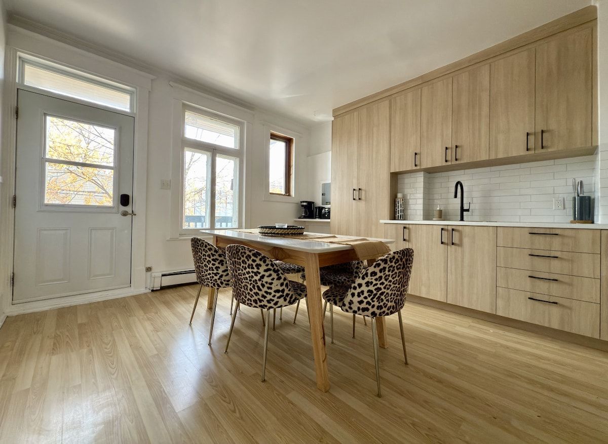 Une cuisine moderne avec des meubles en bois, une table à manger avec des chaises et une fenêtre avec des stores.