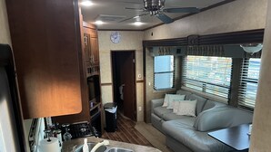 A compact RV interior with a kitchenette, a seating area, and a window with blinds. - Delightful RV in Key Largo, FL (Key Largo)