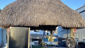 A covered outdoor seating area with a thatched roof, wicker furniture, and a fan. - Delightful RV in Key Largo, FL (Key Largo)