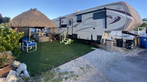 A recreational vehicle (RV) with a "Komfort" branding, parked on a gravel area with a thatched-roof structure nearby. - Delightful RV in Key Largo, FL (Key Largo)