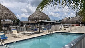 A swimming pool with lounge chairs and thatched umbrellas, surrounded by a fence. - Delightful RV in Key Largo, FL (Key Largo)