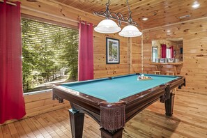 A pool table in a wooden room with a large window, red curtains, and a framed picture on the wall. - PROMO 10% WEEKLY DISCOUNT
Family Cabin Near Dollywood, Hot Tub, Arcade, Pool (Sevierville)