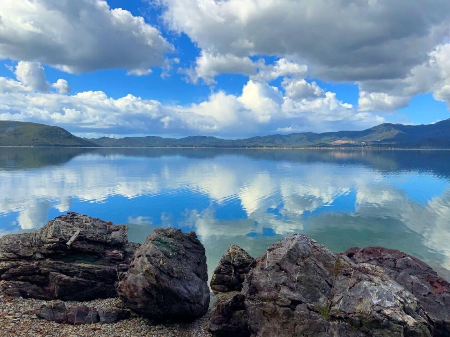 A calm lake with clear reflections of the sky and surrounding mountains.