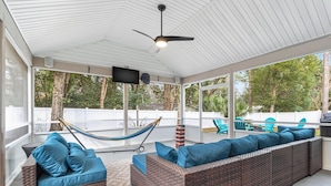 Eine überdachte Terrasse mit Korbmöbeln, einem Deckenventilator und einer Hängematte.