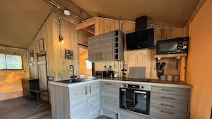 A compact kitchen with wooden cabinetry, a built-in oven, and a microwave. - Lion King Safari Tent (Tenby)