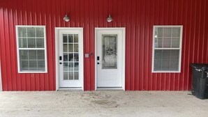 A red building with two white-framed doors and windows, a concrete floor, and a black trash bin. - Country Oasis -B (Hockley)