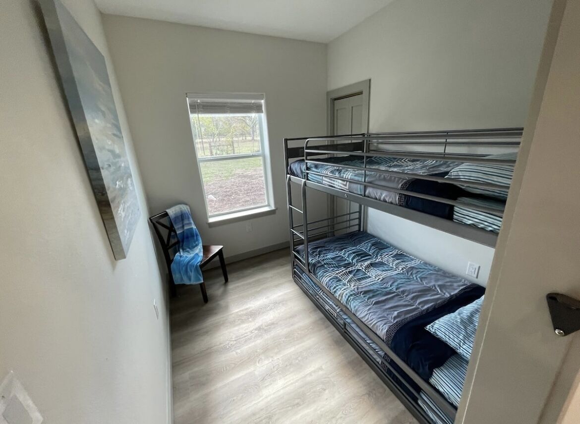 Une pièce avec des lits superposés, une fenêtre, une chaise et une porte.