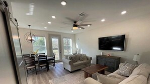 A spacious living room with a dining area, a sofa set, a TV mounted on the wall, and a ceiling fan. - Country Oasis -B (Hockley)