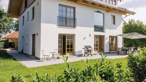 A modern two-story house with a patio area, outdoor seating, and a barbecue grill. - Light-flooded dream home between Chiemsee and the Alps (Traunstein)