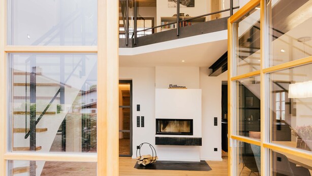 A modern interior with a fireplace, wooden flooring, and a glass railing overlooking a garden. - Light-flooded dream home between Chiemsee and the Alps (Traunstein)