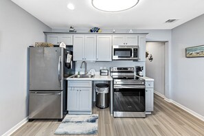 Fully equipped kitchen with stainless steel appliances, refrigerator, microwave, and oven, along with light gray cabinetry and a convenient trash can.