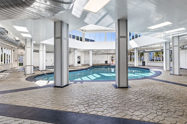 A modern indoor swimming pool with a geometric floor pattern, large windows, and a skylight.