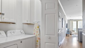 A laundry room with white appliances and a door with a floral curtain. - Pet-friendly oceanfront condo steps from beach & center street (Folly Beach)