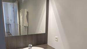 Un bagno con uno specchio grande, un lavandino bianco, un mobile vanitario in legno scuro e un porta asciugamani.