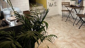 Ein Zimmer mit weißer Ziegelwand, einem Tisch mit Lampe, einer Topfpflanze und einer Wand mit der Aufschrift 'Pink Floyd The Wall'.