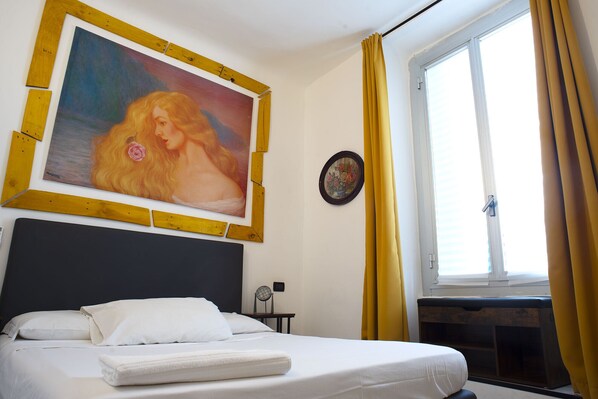 A hotel room with a bed, a painting, a small table with a lamp, and a window with curtains. - RED AND BLUES MUSIC HOTEL GENOVA (Genoa)