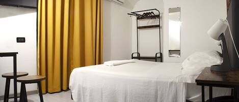 Habitación de hotel con cama, escritorio, silla, espejo y ventana con cortinas amarillas.