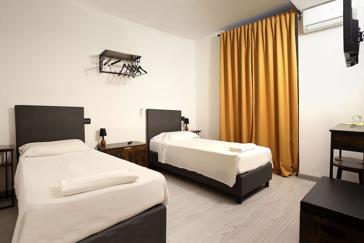 A hotel room with two beds, a wooden nightstand, a desk, and a wall-mounted drying rack.