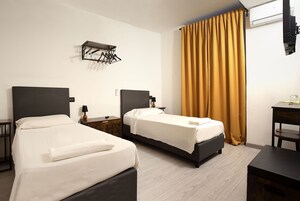 Habitación de hotel con dos camas, una mesita de noche de madera, un escritorio y un tendedero de pared.