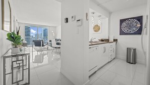 A modern kitchen with white cabinetry, a stainless steel trash can, and a large window offering a city view. - The Club 3305 · *High Floor Superb Unit In the Heart Of Brickell* (Miami)