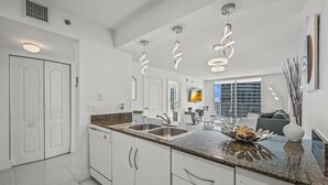A modern kitchen with white cabinets, granite countertops, and a central island. There are pendant lights above the island and a window providing natural light. - The Club 3305 · *High Floor Superb Unit In the Heart Of Brickell* (Miami)