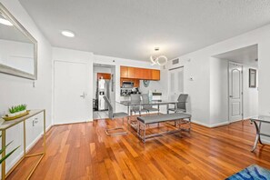 Eine moderne Wohnung mit Holzboden, einem Glastisch und einer Küchenzeile mit Holzschränken.