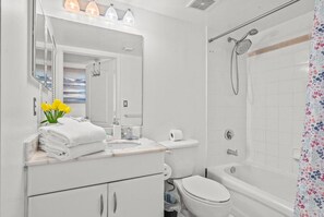 Ein modernes Badezimmer mit Toilette, Waschbecken und Dusche. Handtücher liegen auf dem Waschbecken und darüber befindet sich ein Spiegel.